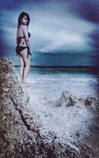 Young woman standing at beach against sky