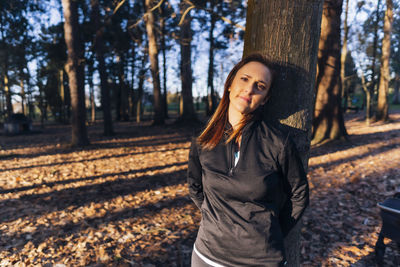 Portrait of young woman standing on tree trunk