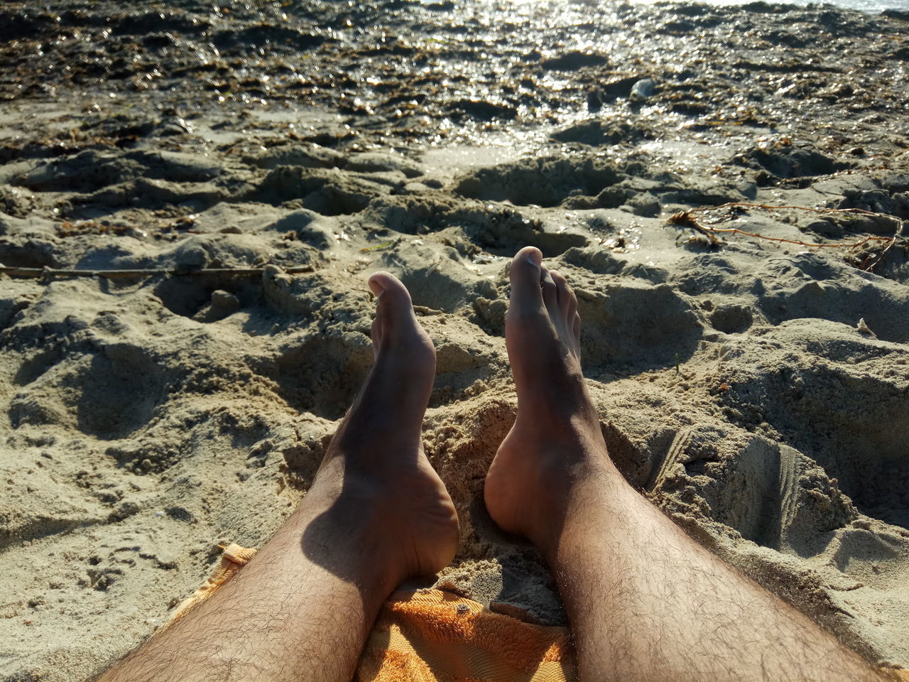 LOW SECTION OF MAN RELAXING ON SHORE