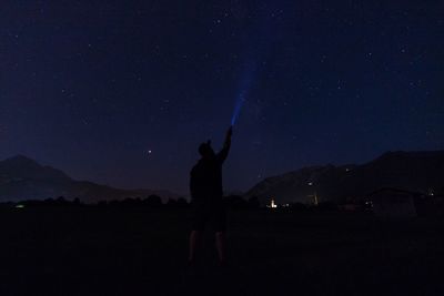 Silhouette man holding flashlight while standing on field against sky at night