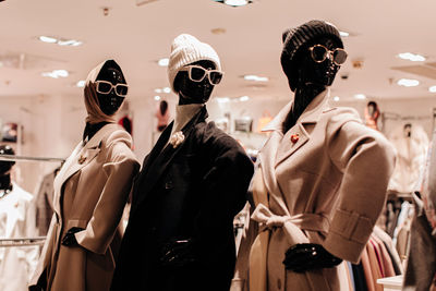 Three mannequins in a store window dressed in seasonal fashion cloth. beige and black long coats