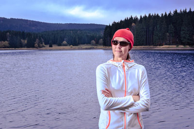 Woman wearing sunglasses while standing by lake against sky