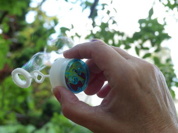 Cropped hand holding bubble wand against trees