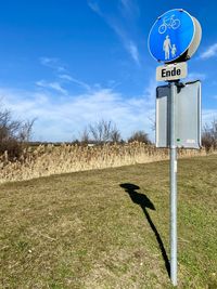 Road sign on field against sky