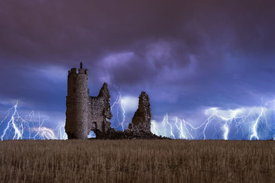 Amazing scenery of lightning storm on colorful cloudy sky over ruined old castle at night