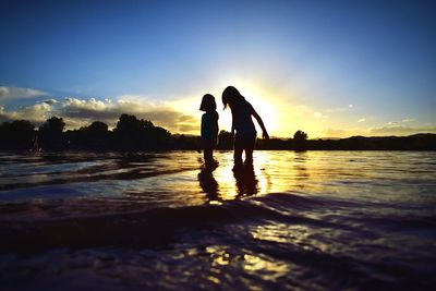 Silhouette people by swimming pool against sky during sunset