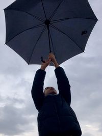 Low angle view of boy holding umbrella against sky