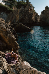 Woman sitting on rock formation by sea