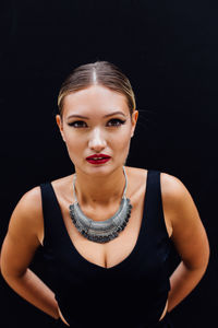 Portrait of young woman standing against black background