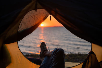 Low section of man relaxing on sea during sunset