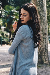 Side view of young woman standing against tree