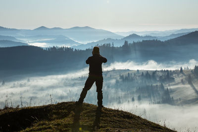 Rear view of man standing on mountain against sky