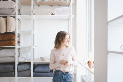 Smiling female entrepreneur holding mobile phone while looking through window in upholstery store