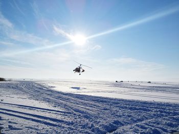 Helicopter flying over snow covered landscape against sky