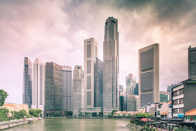 Modern buildings by river against sky in city