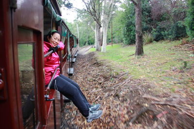 Full length portrait of happy woman sitting in train at forest