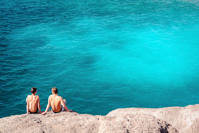 Rear view of two people sitting on shore