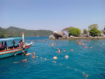 People on boats in sea against clear blue sky