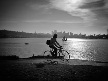 Buildings against the sky with man bicycling by calm river