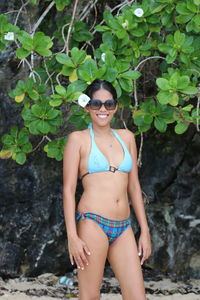 Portrait of smiling young woman in bikini standing against trees