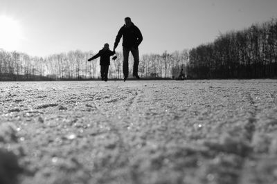 Father and son ice skating against sky