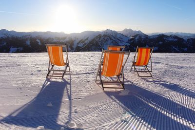 Deck chairs on snowcapped mountain against sky during winter