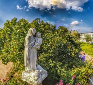 Statue in front of garden against sky