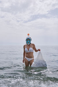 A young girl with diving goggles pulling trash out of the ocean. recycling concept