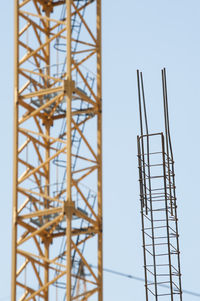 Low angle view of crane and iron rods at incomplete building against clear sky