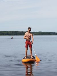 Full length of shirtless man standing in sea against sky