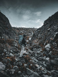 Man on rocks by mountains against sky