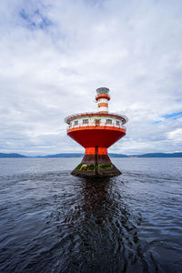 Red lighthouse by sea against sky