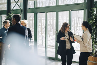 Business colleagues communicating while standing against window at office