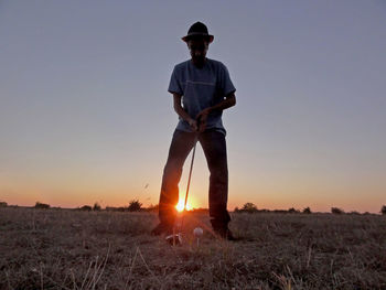 Low angle view of man playing golf on field against clear sky during sunset