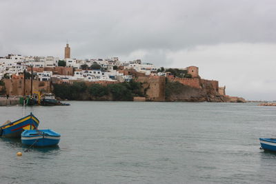 Boats moored on sea by buildings in city against sky