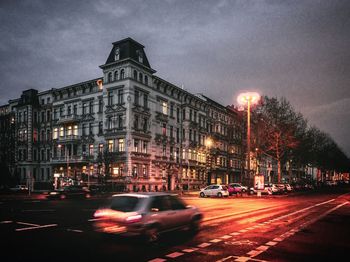 Cars on road by buildings against sky at night