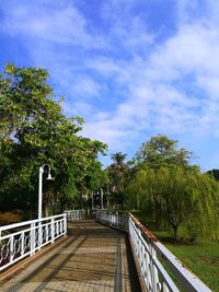 Footbridge amidst trees in city against sky