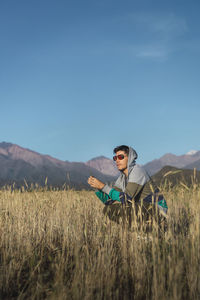 Young man with sunglasses sitting on in field looking at mountains wit