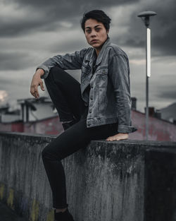 Portrait of woman sitting on retaining wall against sky