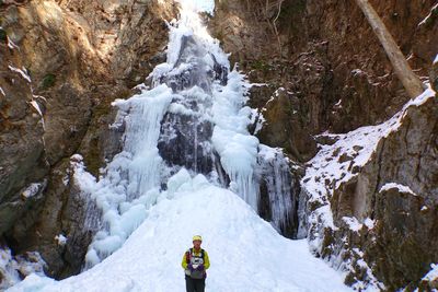 Man standing on snow covered land against rock formation