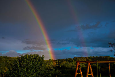 Rainbows over field against cloudy sky