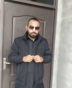 Portrait of young man wearing sunglasses standing against wall