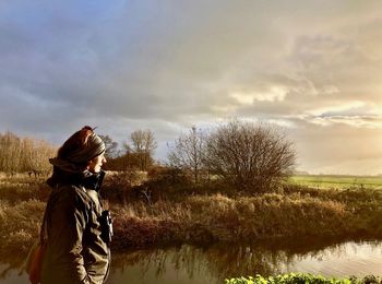 Woman standing by lake against cloudy sky during sunset