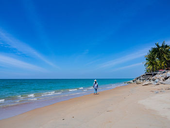 A tourist walking on beautiful sandy palm beach with blue sky and sea waves in sunny summer day