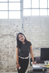 Portrait of confident female computer programmer standing beside desk at creative office