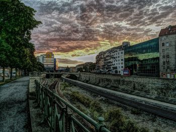 Railroad tracks amidst buildings in city against sky during sunset