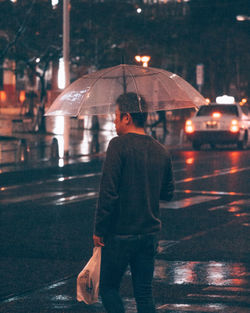 Rear view of woman standing on wet road at night