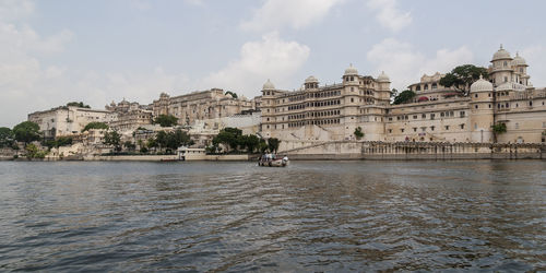 Buildings at waterfront against cloudy sky