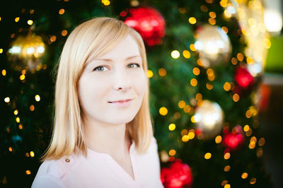 Close-up portrait of young woman smiling while standing by christmas tree