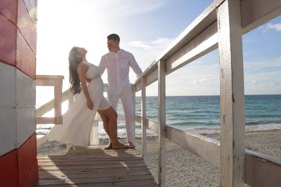 Full length of romantic couple by railing at beach